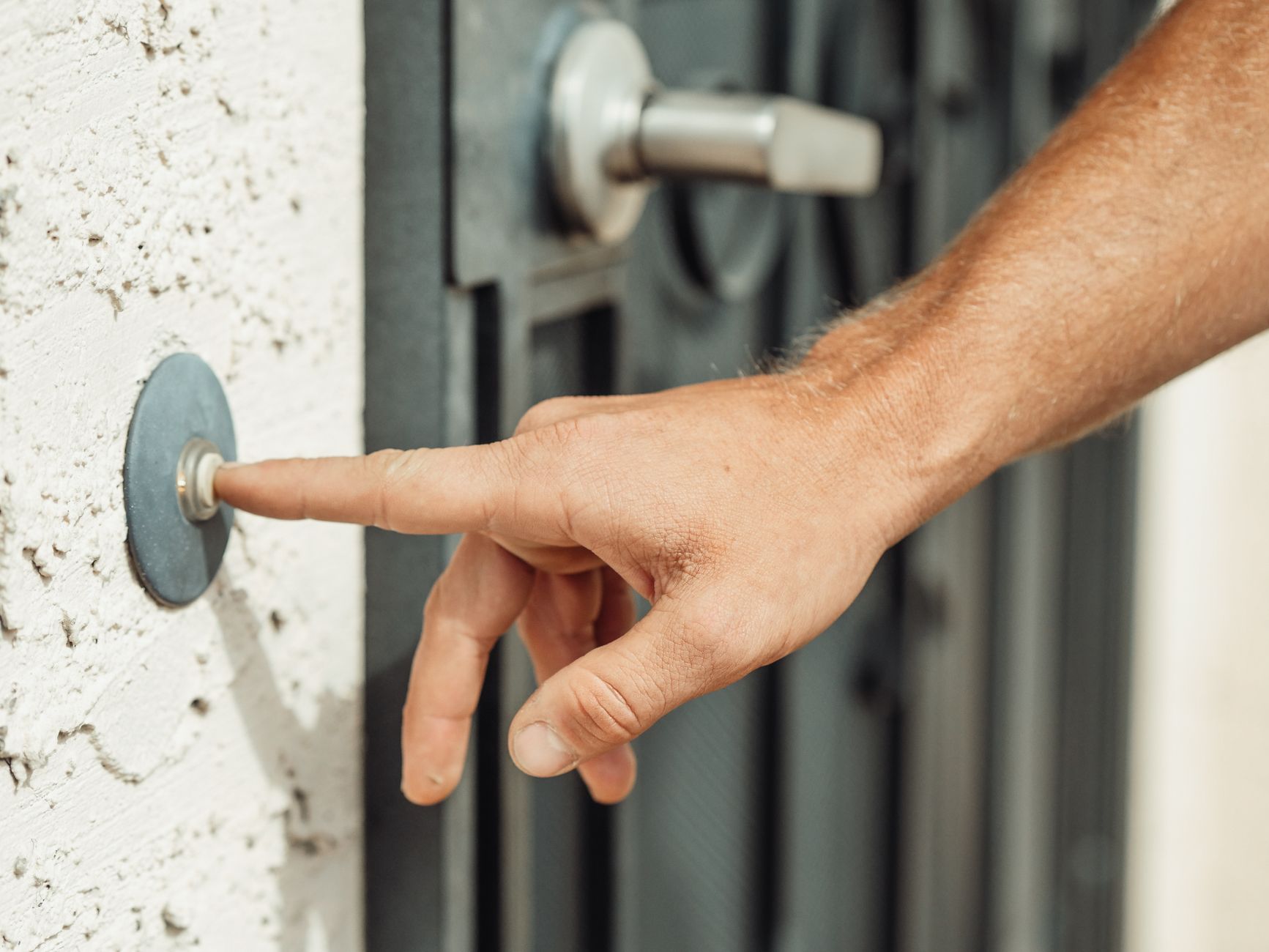 Hand pressing a doorbell at a residential entry.